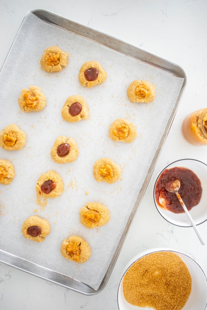 sourdough jam thumbprint cookies on a baking sheet on a marble counter.