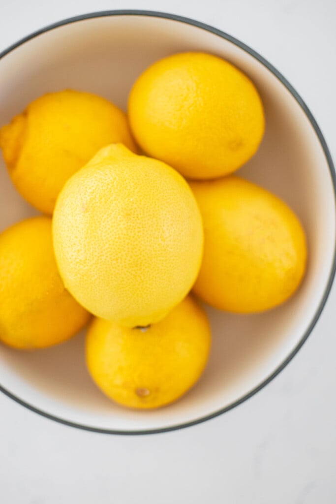 lemons in a white bowl on a white marble counter.