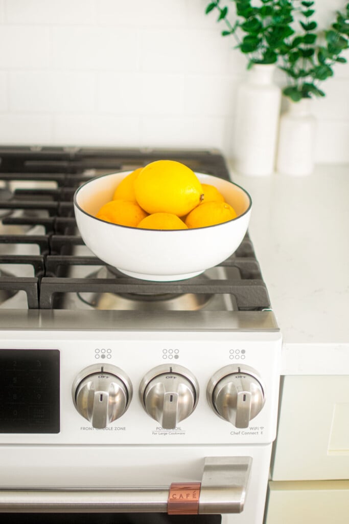 lemons in a white bowl sitting on top of a white oven.