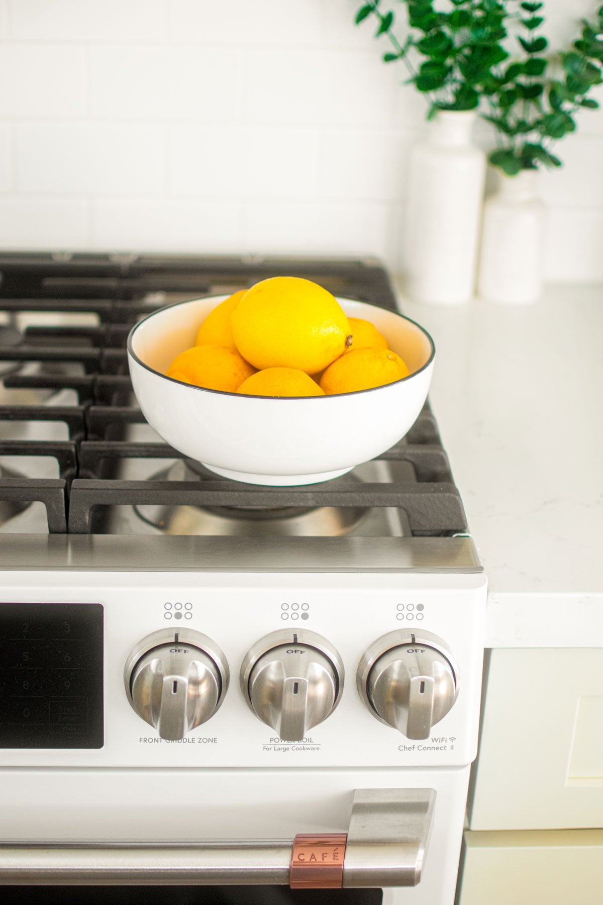 lemons in a white bowl sitting on top of a white oven.
