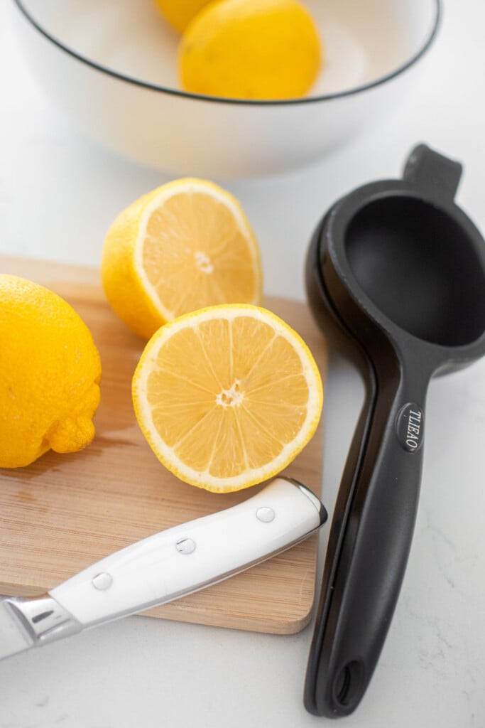 lemons cut in half on a wood board with a black juicer on a white marble counter.