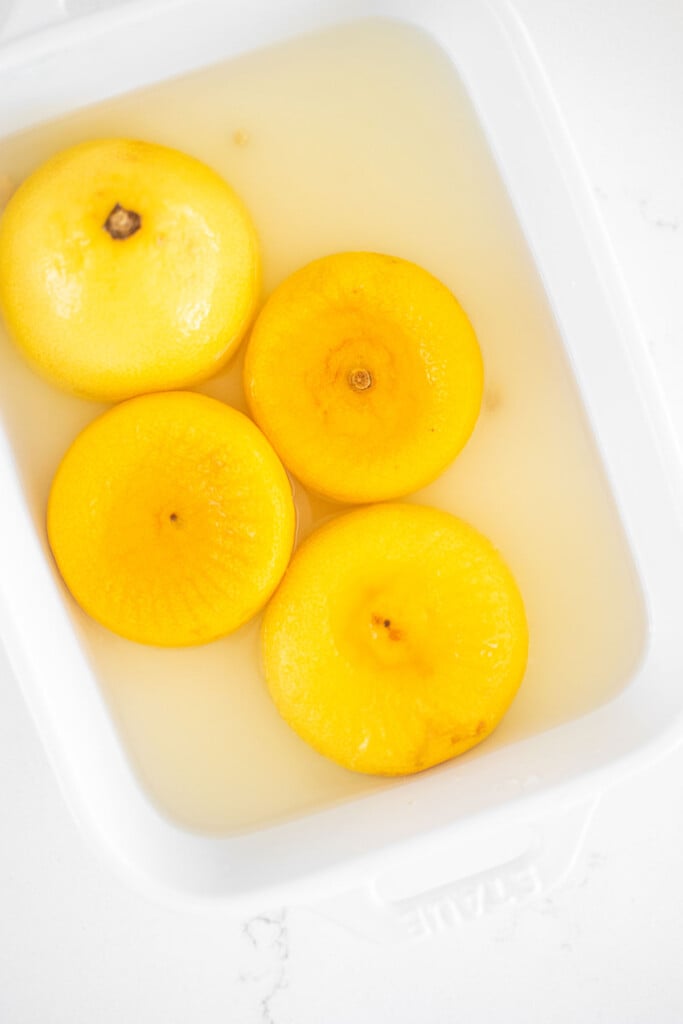 lemons juiced in water in a white ceramic dish on a marble counter.