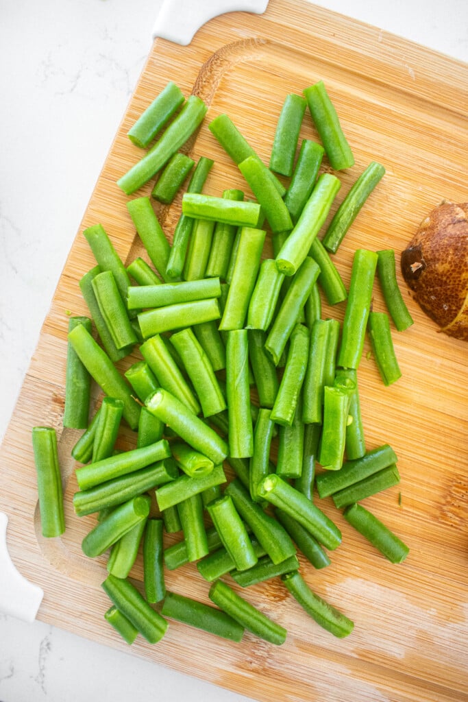 chopped green beans on a wood cutting board on a marble countertop.