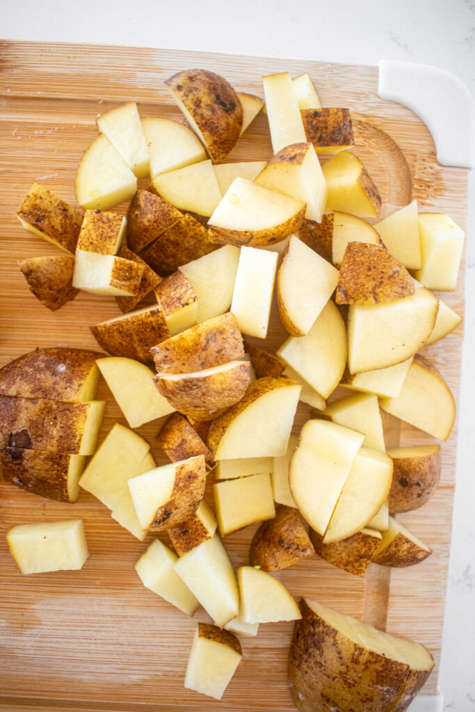 chopped potatoes on a wood cutting board on a marble countertop.