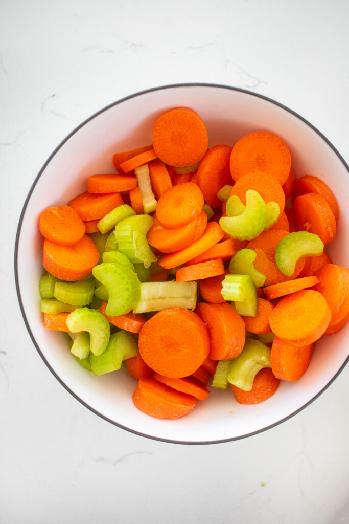 chopped carrots and celery in a bowl on a marble countertop.