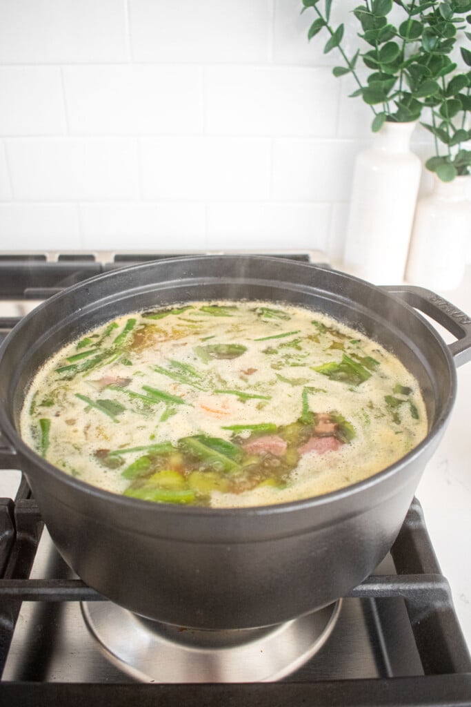 ham bone soup simmering in a dutch oven on a stovetop.
