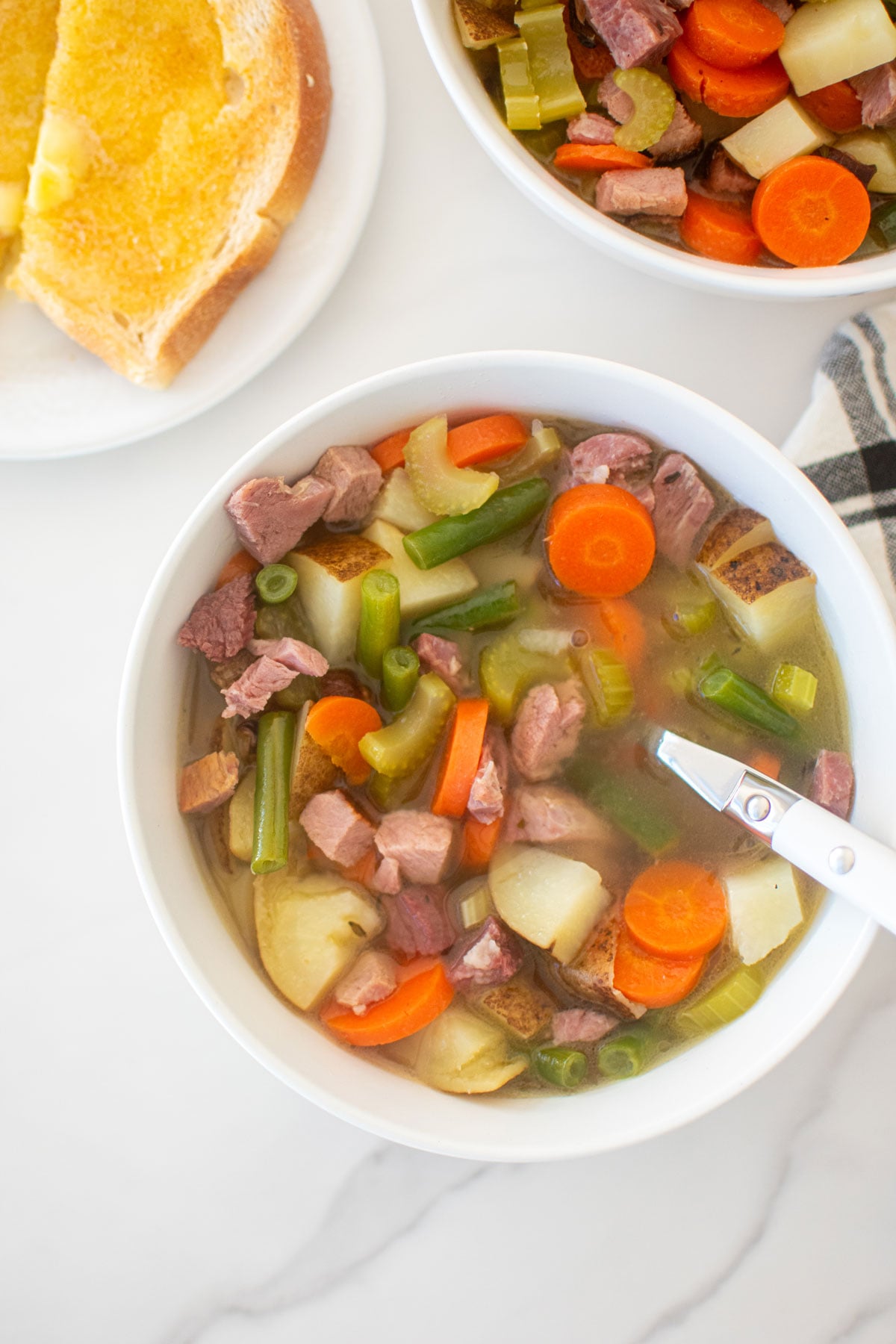 ham bone soup in a bowl with a small plate and toast on the side on a marble countertop.