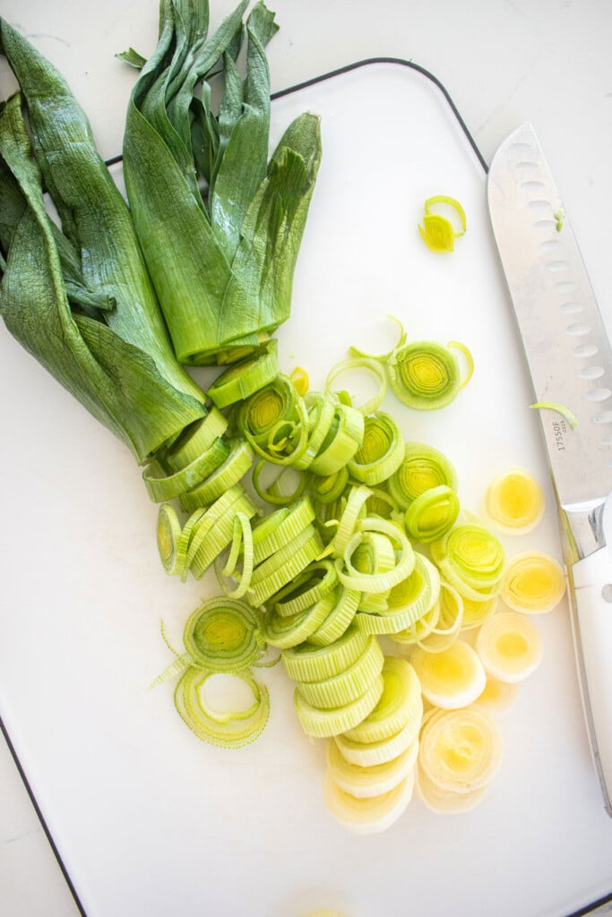 sliced leeks on a white cutting board on a marble countertop.