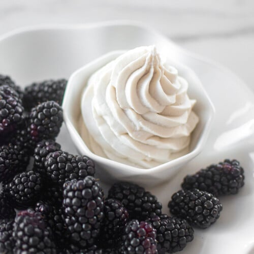 homemade organic vegan whipped cream piped into a small dish with fresh blackberries on a marble table.