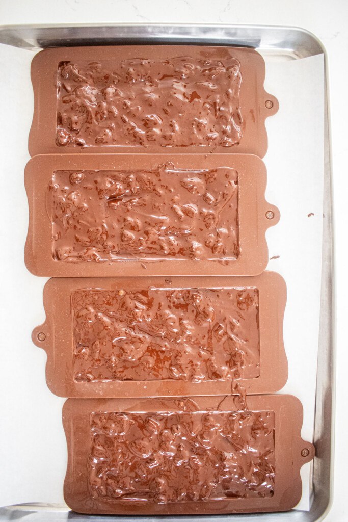 salted almond dark chocolate bars in chocolate molds on a baking sheet.