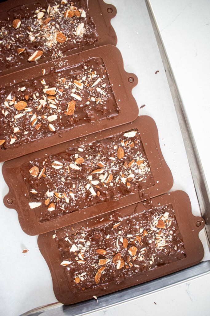 salted almond dark chocolate bars in chocolate molds on a baking sheet.