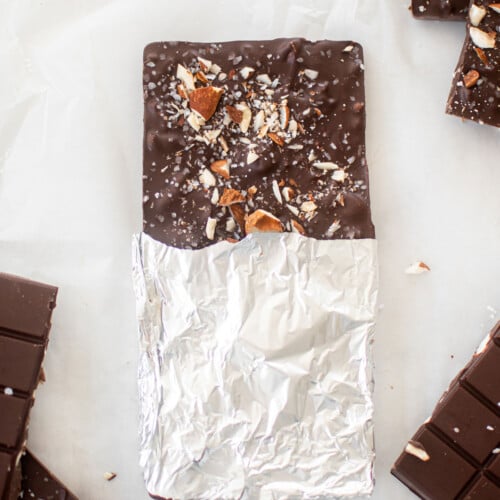 salted almond dark chocolate bar wrapped in foil on a white marble counter.