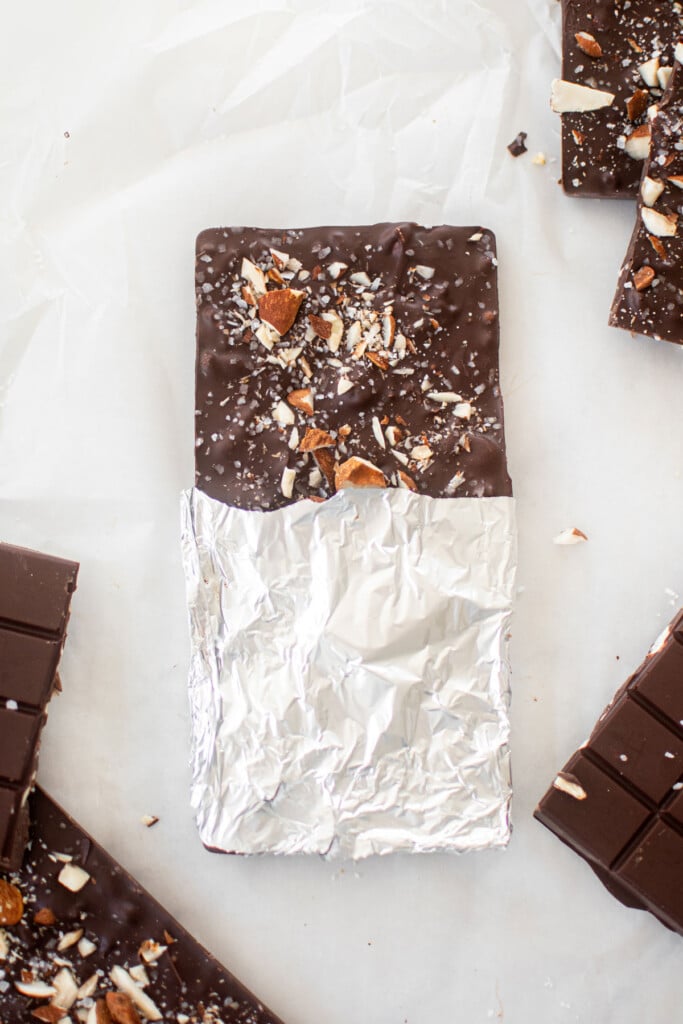 salted almond dark chocolate bar wrapped in foil on a white marble counter.
