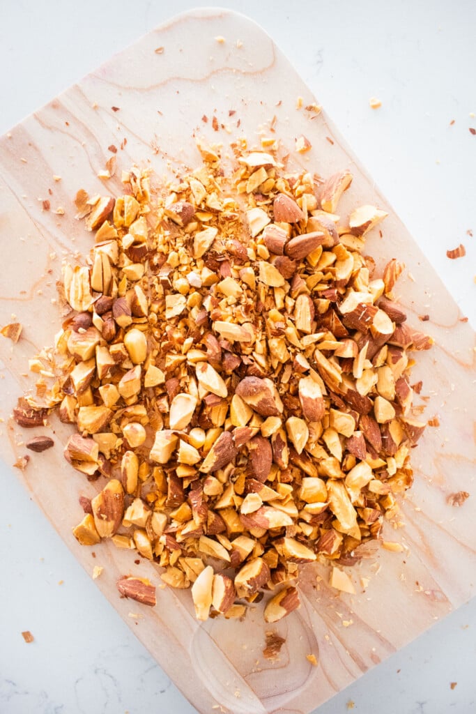 chopped almonds on a wood cutting board on a marble counter.