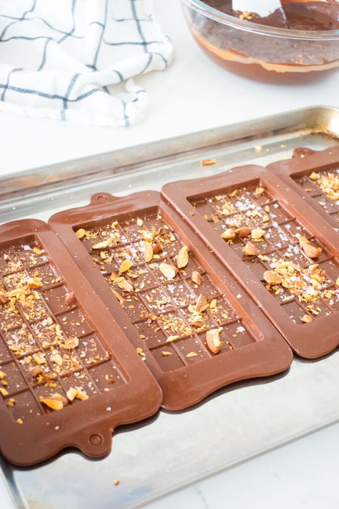 chocolate bar molds on a baking sheet with chopped almonds on a marble counter.
