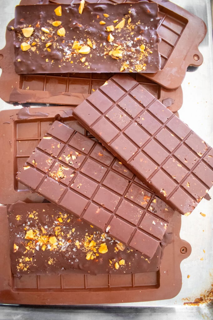 salted almond dark chocolate bars on a baking sheet being removed from chocolate molds.