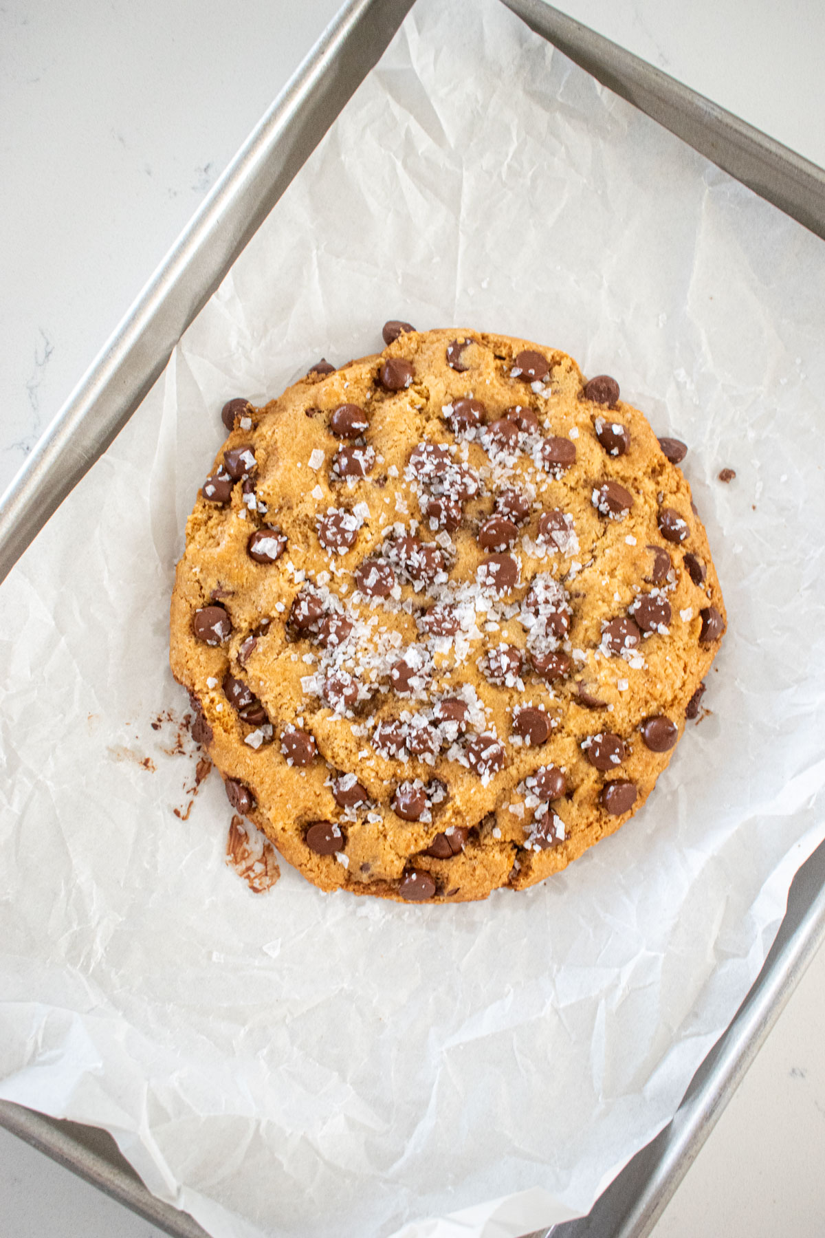 single serve chocolate chip cookie with sea salt on a baking sheet on a marble counter.