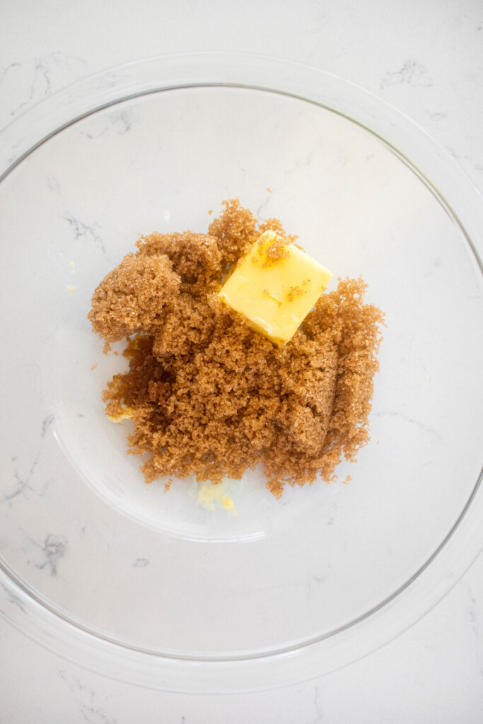 butter, brown sugar and vanilla in a glass mixing bowl on a marble counter.