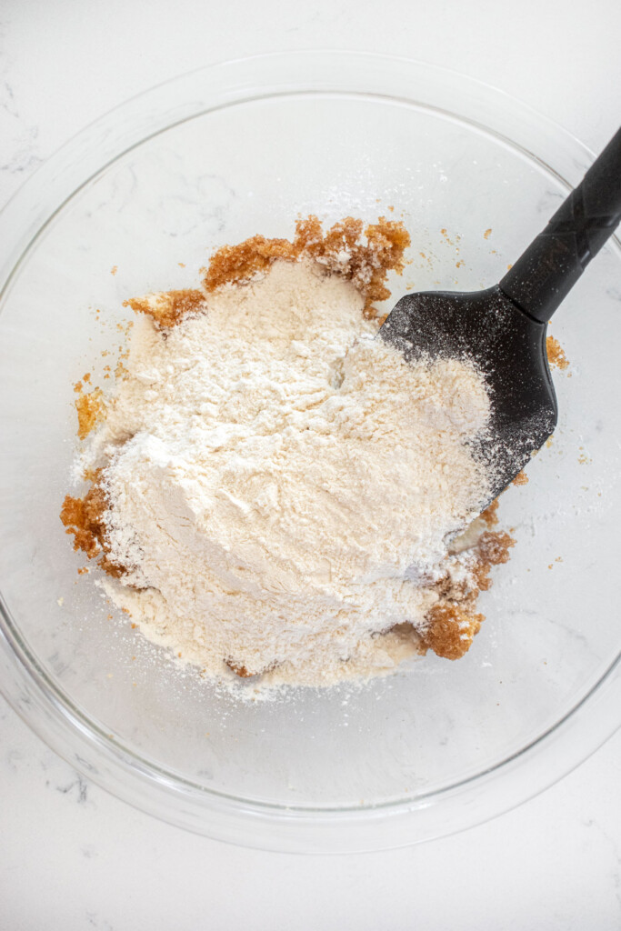ingredients for single serve cookie dough in a glass mixing bowl on a marble counter with a spatula.