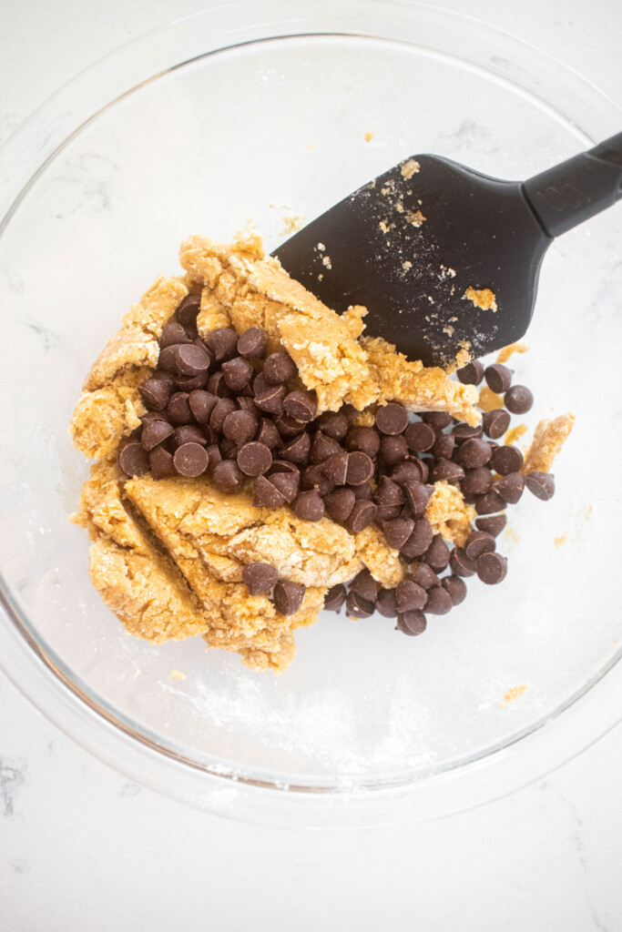 single serve cookie dough with chocolate chips in a glass mixing bowl on a marble counter with a spatula.