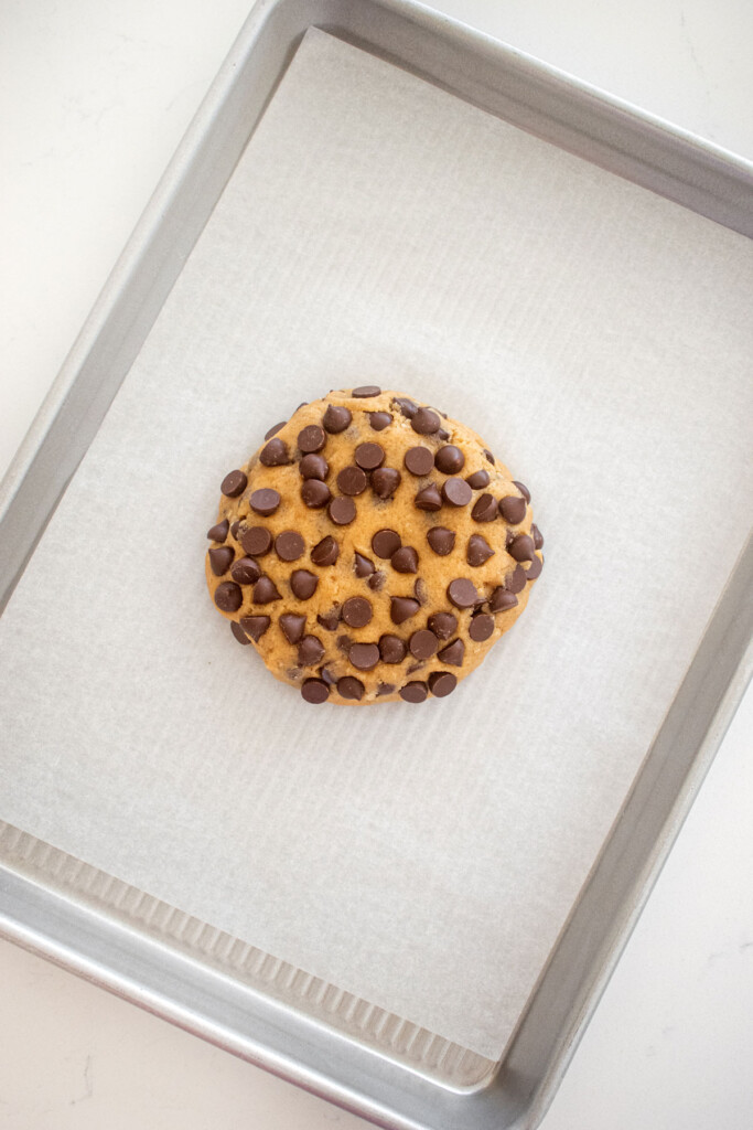 single serve chocolate chip cookie on a baking sheet on a marble counter.