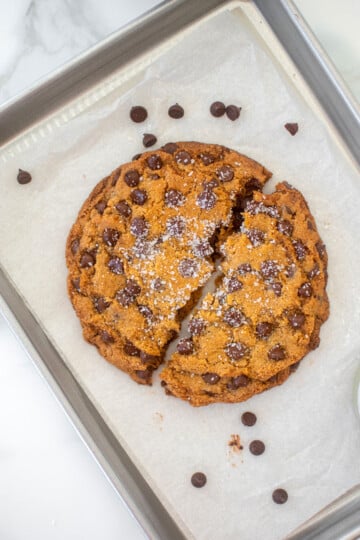 single serve chocolate chip cookie broke in half on a small baking sheet on a marble counter.