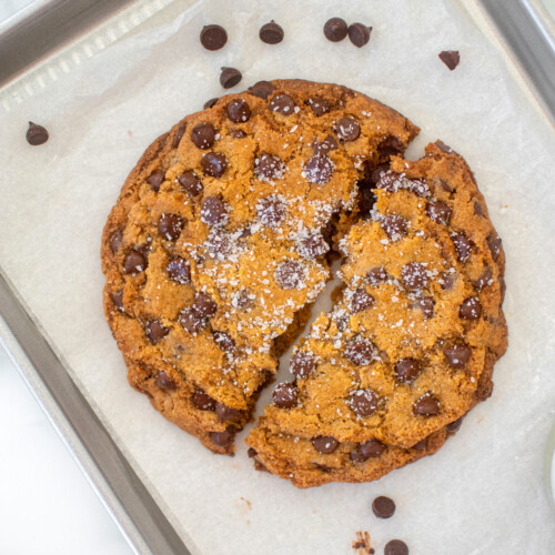 single serve chocolate chip cookie broke in half on a small baking sheet on a marble counter.