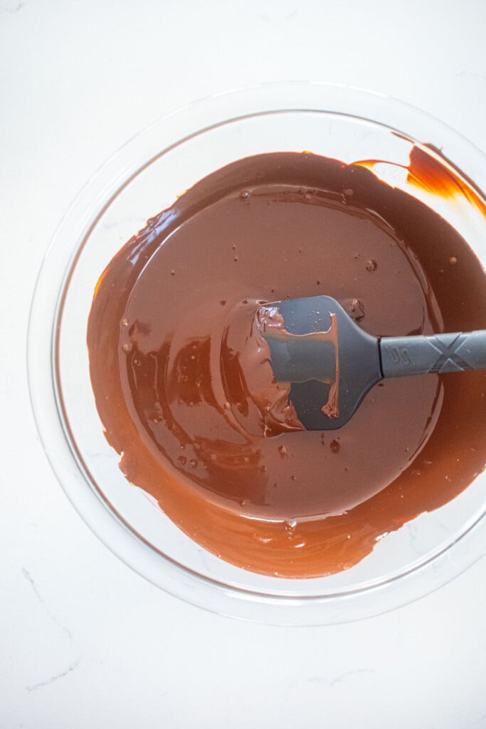 melted chocolate in a glass mixing bowl on a marble countertop.