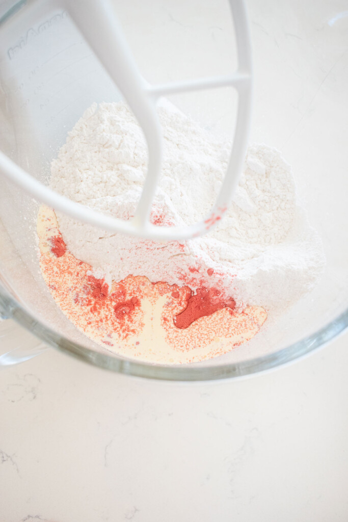 ingredients for strawberry cream drops in a glass mixing bowl on a white marble counter.
