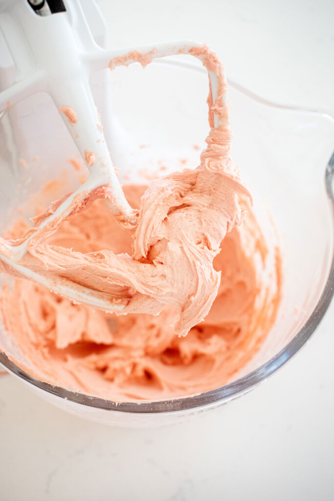strawberry buttercream filling mixed in a glass mixing bowl on a white marble counter.