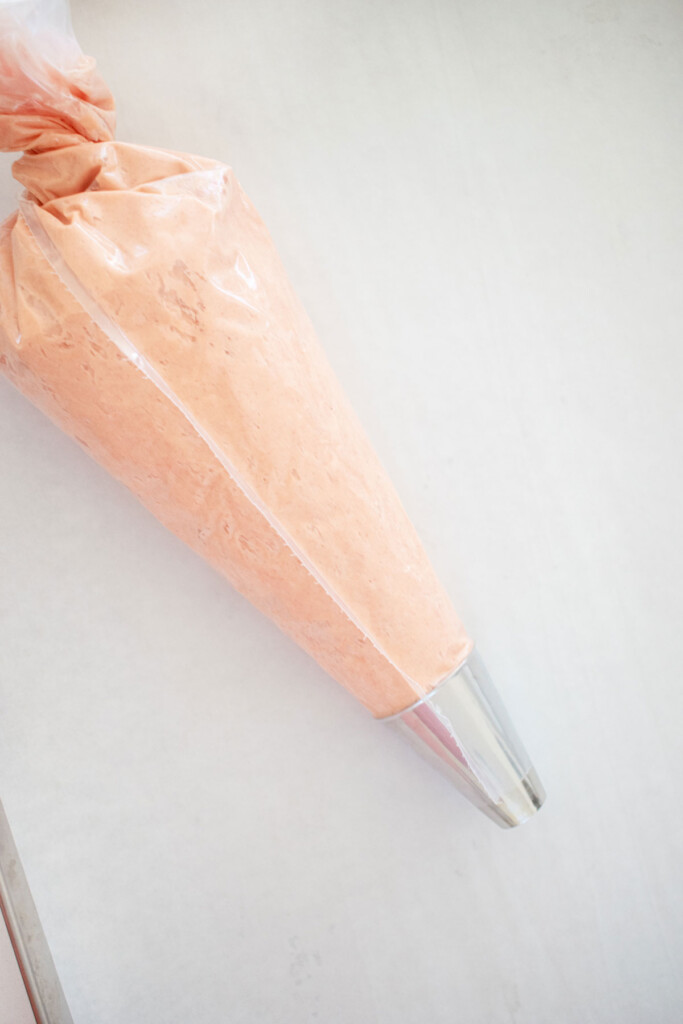 strawberry buttercream filling in a piping bag on a white parchment paper lined baking sheet.