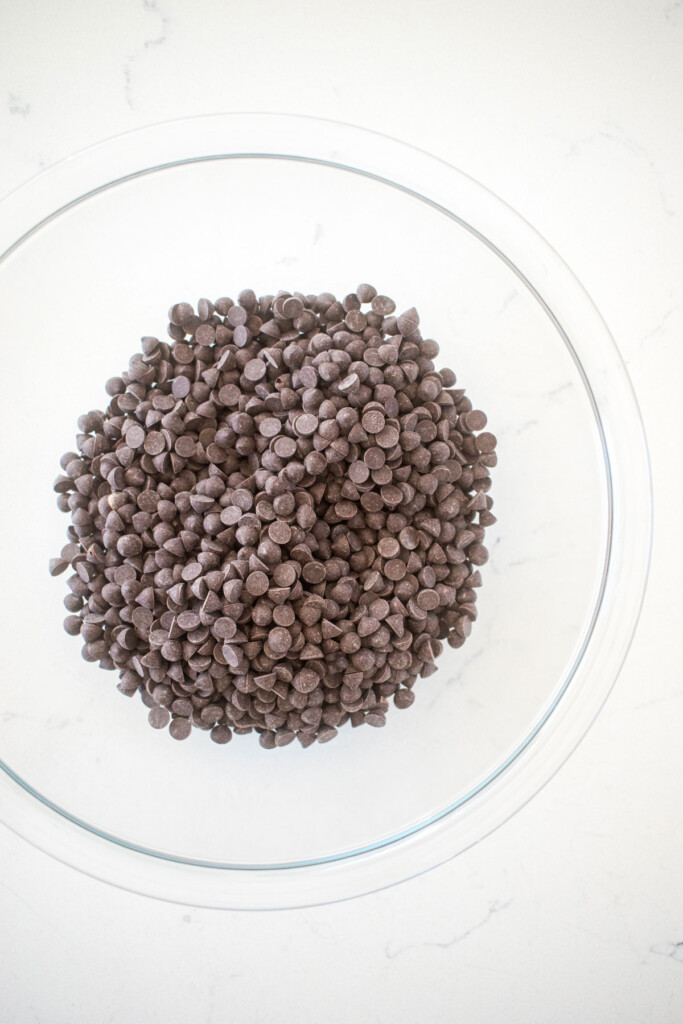 mini dark chocolate chips in a glass mixing bowl on a white marble counter.