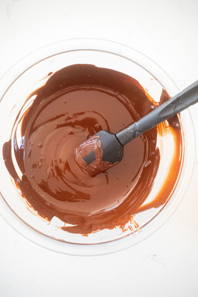 melted dark chocolate in a glass mixing bowl on a marble counter.