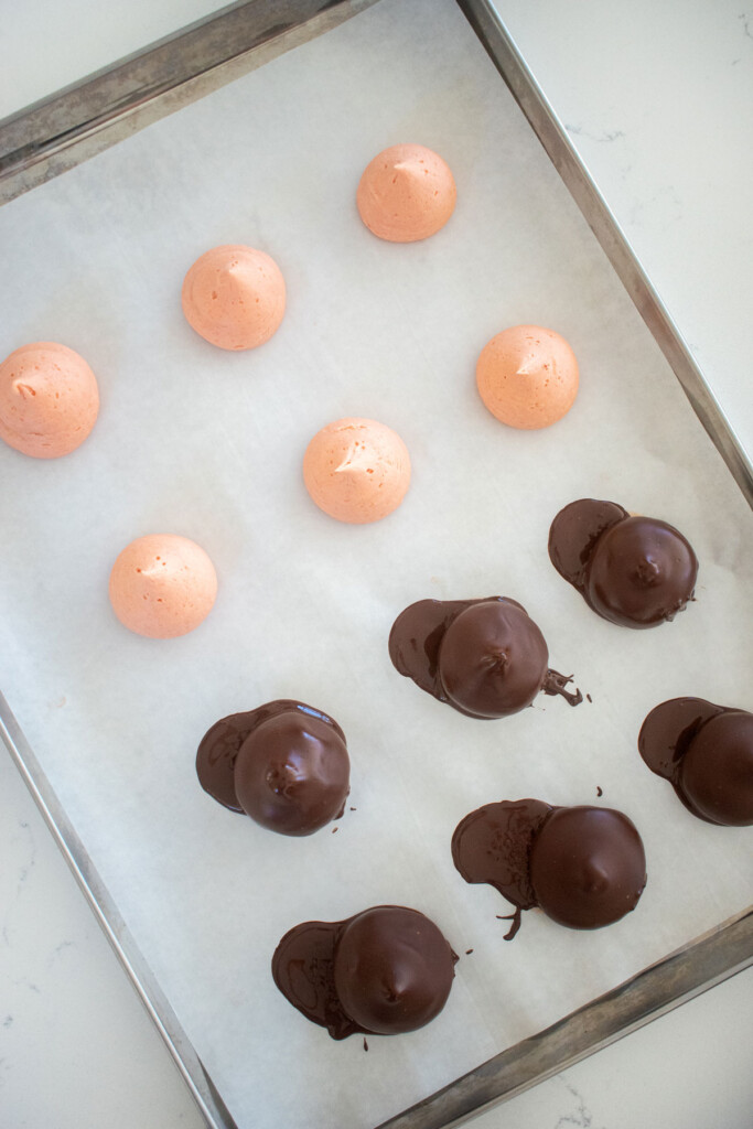 strawberry cream drops on a baking sheet being covered in dark chocolate on a marble counter.