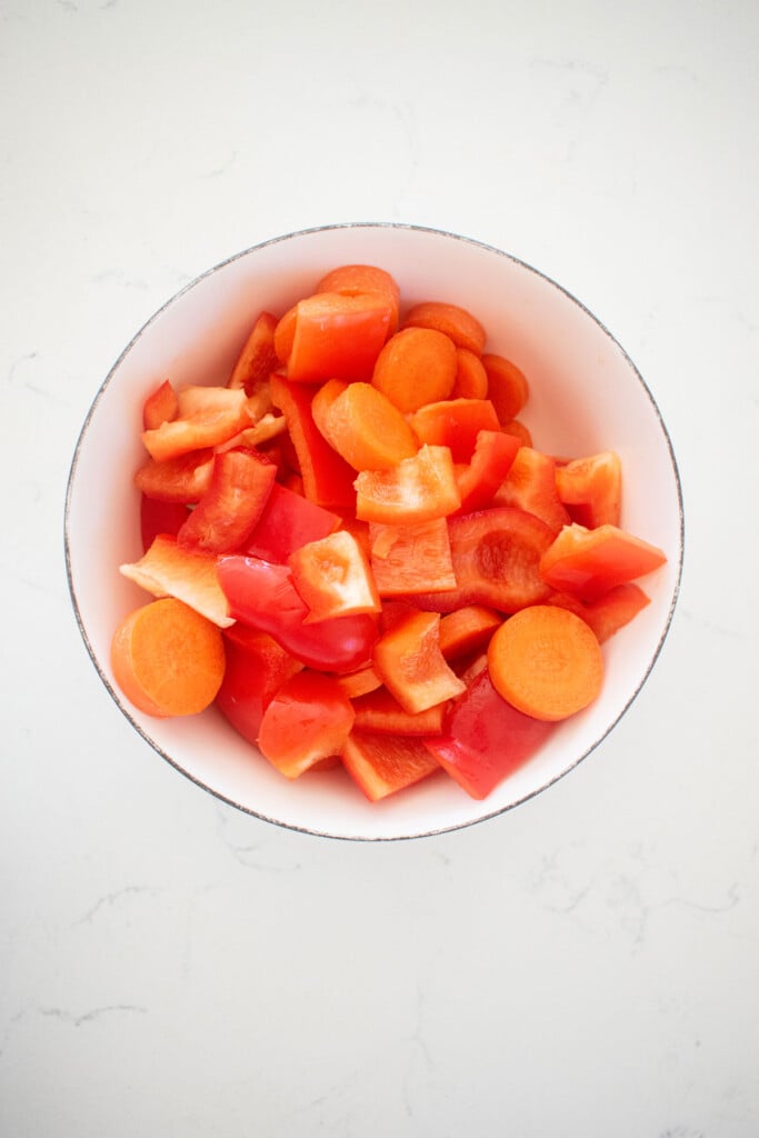 chopped red bell peppers and carrots in a bowl on a white countertop.