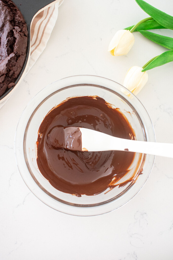 melted chocolate in a small glass mixing bowl on a white marble counter with white tulips.