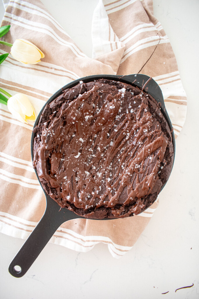 bone broth brownies in a skillet with melted chocolate drizzle on top and flakey sea salt on a white marble counter.