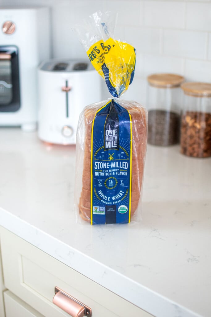 one mighty mill whole wheat bread loaf sitting on a white marble countertop with toaster in the background.