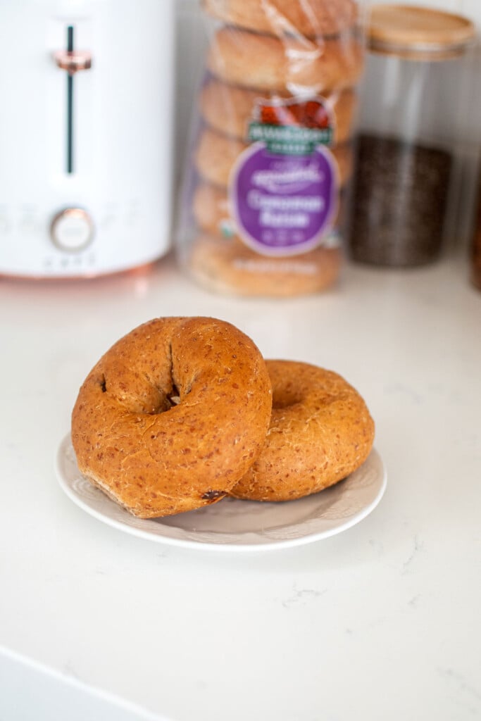 cinnamon raisin bagels on a plate on a marble countertop in front of a toaster.