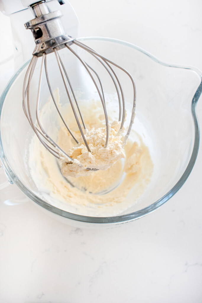 whipped cream in a glass mixing bowl on a white marble counter.