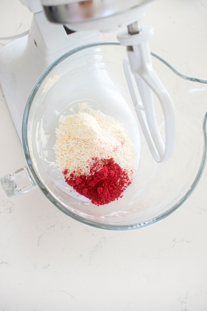 ingredients for raspberry truffles in a glass mixing bowl on a white marble counter.