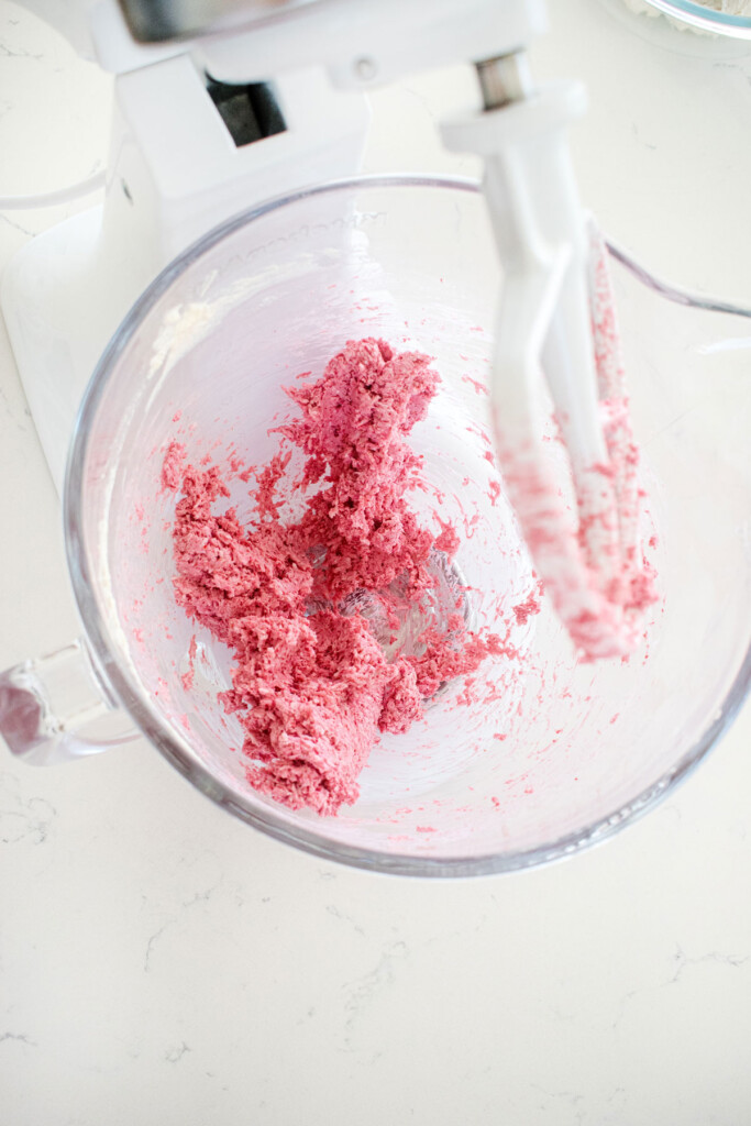 raspberry truffles being mixed in a glass mixing bowl on a white marble counter.