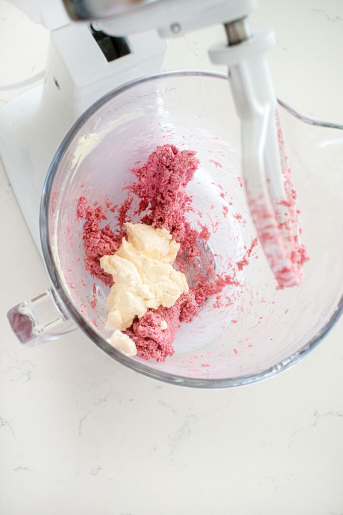 raspberry truffles being mixed in a glass mixing bowl on a white marble counter.