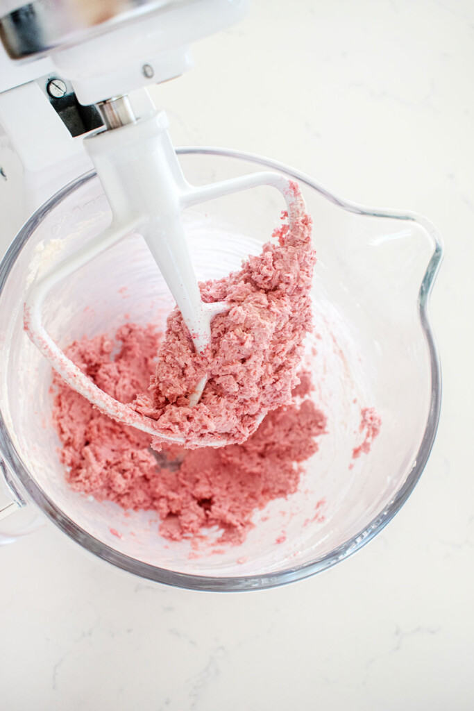 raspberry truffles being mixed in a glass mixing bowl on a white marble counter.