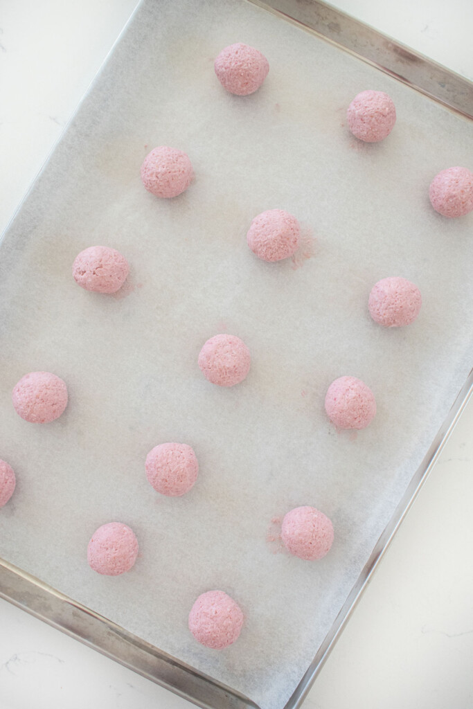 raspberry truffles rolled into balls on a baking sheet.