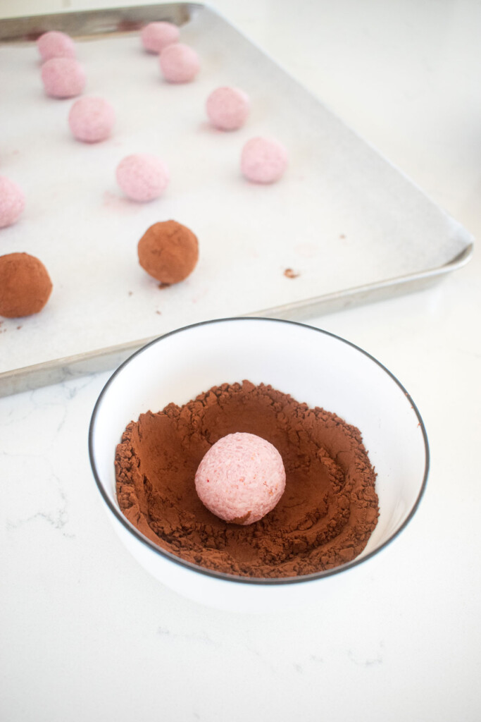 raspberry truffle in a bowl of cocoa powder on a white marble counter.