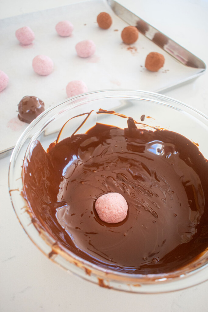raspberry truffle in a bowl of dark chocolate on a white marble counter.