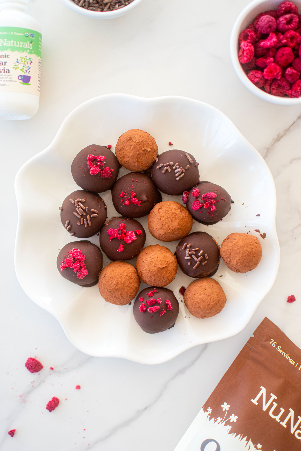white ruffle plate of raspberry truffles on a white marble counter.