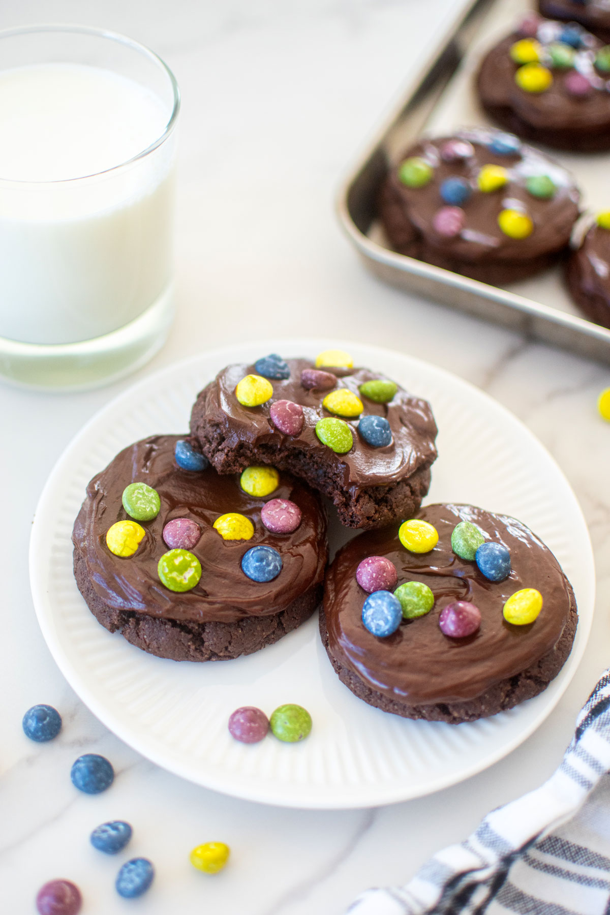 plate of eggless cosmic brownie cookies and a glass of milk on a marble counter.