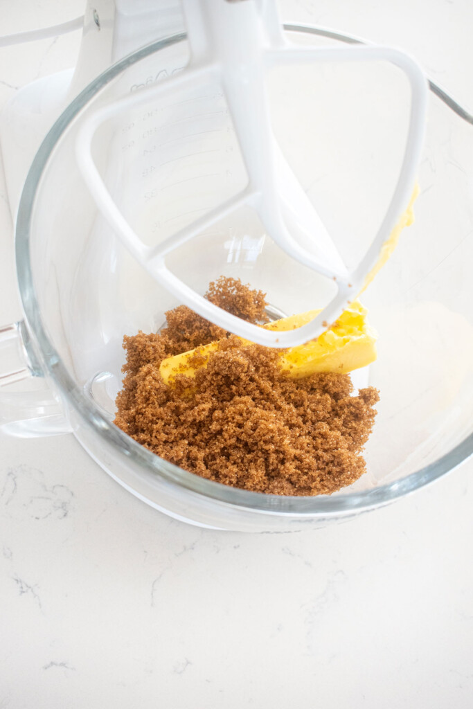 butter and brown sugar in a glass mixing bowl on a marble counter.